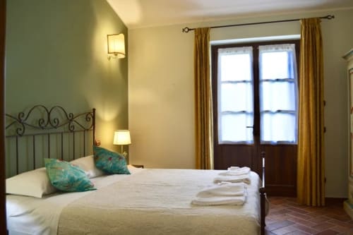 Il Gelsomino bedroom at Agriturismo Colle Mura with iron bed, turquoise pillows, and terracotta floors in Gualdo Tadino