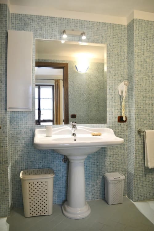 Bagno moderno con rivestimento in mosaico, lavabo su colonna e ampio specchio presso l'Agriturismo Colle Mura a Gualdo Tadino