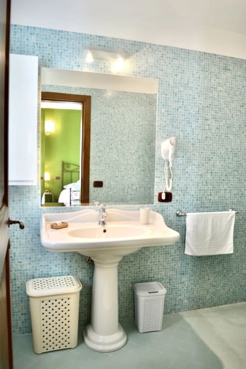 Bagno moderno nella stanza Il Glicine dell'Agriturismo Colle Mura di Gualdo Tadino, con piastrelle a mosaico blu e lavabo su colonna