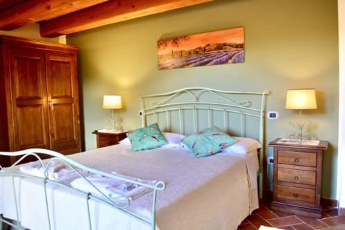 La Lavanda room at Agriturismo Colle Mura in Gualdo Tadino, featuring iron bed, lavender decor, wooden beams, and countryside