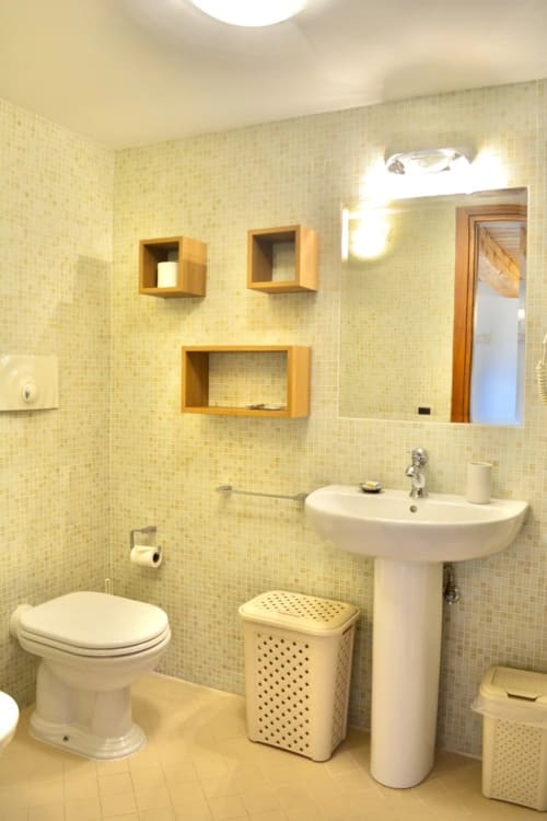 Bagno luminoso all'Agriturismo Colle Mura di Gualdo Tadino con piastrelle gialle, lavabo su colonna, wc e scaffali in legno