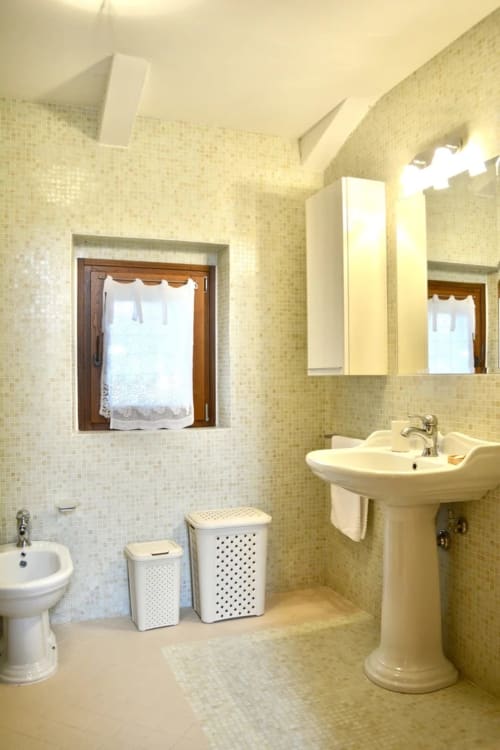 Bagno luminoso dell'Agriturismo Colle Mura a Gualdo Tadino con lavandino a colonna, wc, finestra e cesti bianchi per la biancheria