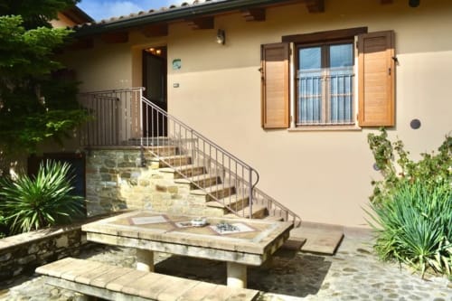 Cortile della camera L'Abete presso l'Agriturismo Colle Mura a Gualdo Tadino, con patio in pietra, tavolo da pranzo e finestre con persiane
