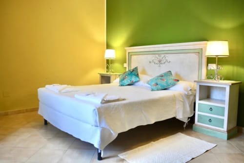 Camera luminosa all'Agriturismo Colle Mura a Gualdo Tadino con pareti gialle e verdi, letto bianco e cuscini turchesi
