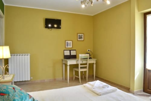 Camera luminosa giallo sole presso l'Agriturismo Colle Mura con letto, scrivania, radiatore e soffitto bianco a Gualdo Tadino