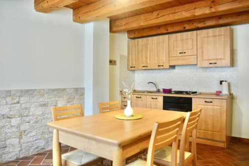 Rustic kitchen and dining area at Agriturismo Colle Mura in Gualdo Tadino with wooden beams, stone accent wall, and four-seat