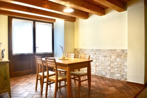 Dining area in Il Noce apartment at Agriturismo Colle Mura, Gualdo Tadino, with wooden table, chairs, exposed beams, and
