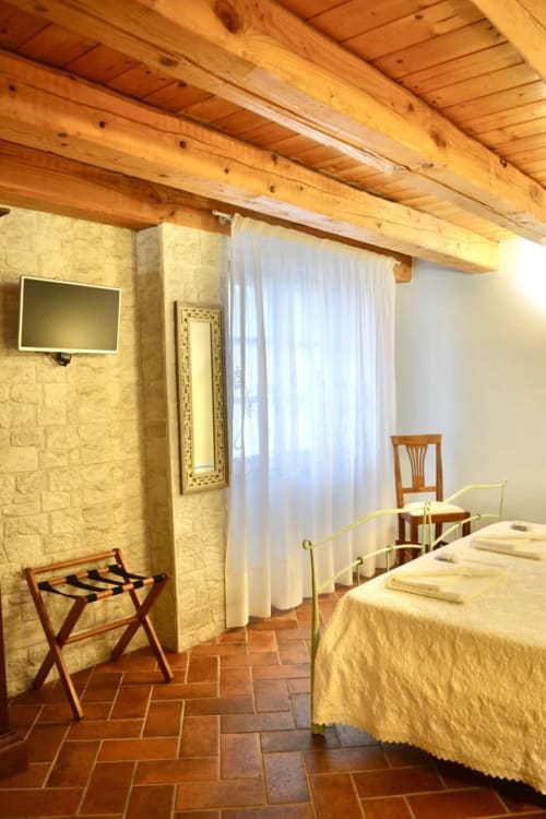 Rustic bedroom at Agriturismo Colle Mura with wooden beams, terra cotta floors, and yellow linens in Gualdo Tadino, Italy