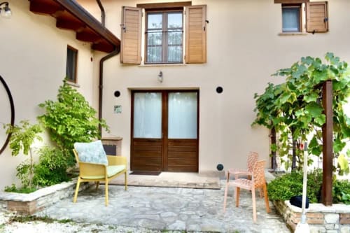 Courtyard at Agriturismo Colle Mura in Gualdo Tadino with wooden doors, climbing vines, yellow chair, and stone patio
