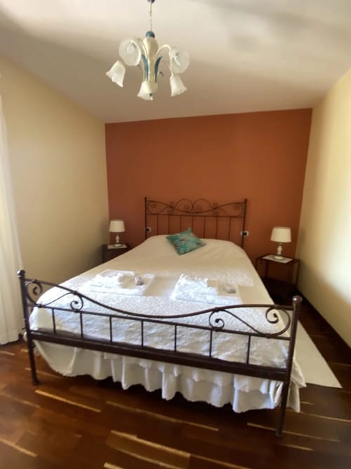 Camera da letto ad Agriturismo Colle Mura con letto in ferro battuto, parete in cotto e biancheria crema a Gualdo Tadino