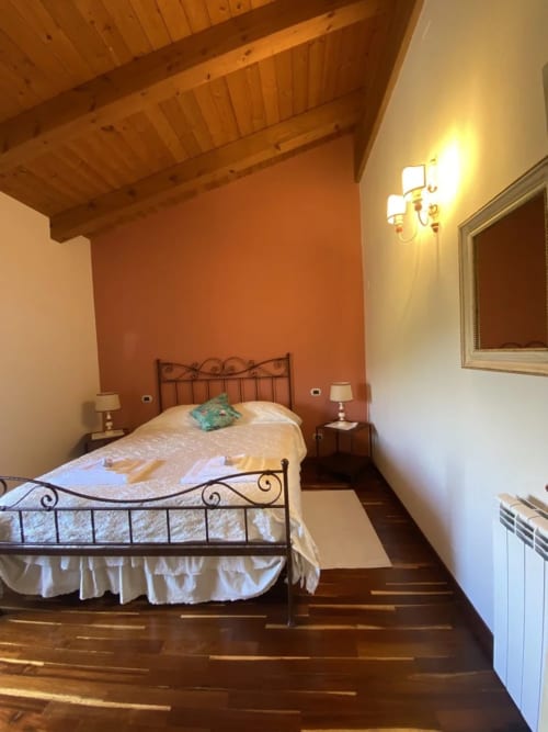 Camera accogliente all'Agriturismo Colle Mura con letto in ferro battuto, travi di legno e parete color arancio caldo a Gualdo Tadino