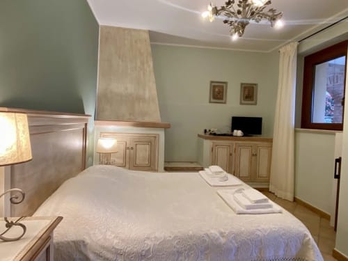 Le Campanule room at Agriturismo Colle Mura in Gualdo Tadino, featuring a bed with white linens, wooden furnishings, and sage