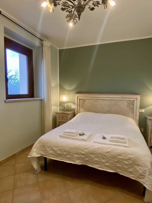 Le Campanule bedroom at Agriturismo Colle Mura in Gualdo Tadino with sage walls, wooden bed, and natural light