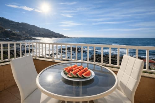 Terraza frente al mar en la casa Holibai de Baiona con mesa redonda, rodajas de sandía, vista al mar y barandilla blanca