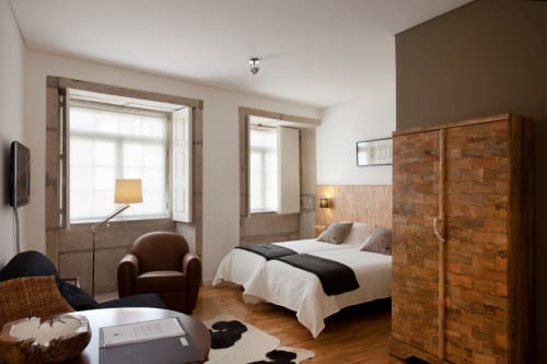 Quarto moderno do hotel PortoSense Porto com móveis de madeira, duas cama solteiro ou cama de casal, poltrona e amplas janelas com vista cidade e rio.
