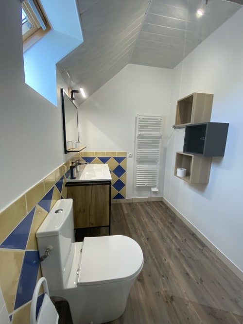 Modern bathroom at Domaine des Piéris in Grandcamp-Maisy with geometric tile backsplash, toilet, sink, skylight, and wooden