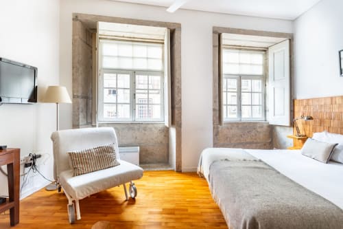 Quarto brilhante no PortoSense Porto com piso de madeira, cama de casal, poltrona e amplas janelas com vista para a cidade.