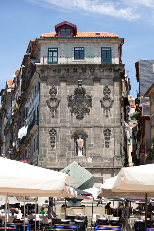 Fachada histórica de edifício em pedra com detalhes ornamentais no centro antigo do Porto, com esplanada abaixo