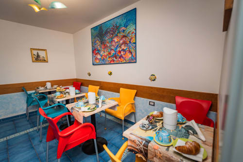Sala colazioni vivace di Casa Mannini B&B a Maiori con sedie colorate, tavoli per la prima colazione e dipinti artistici alle pareti