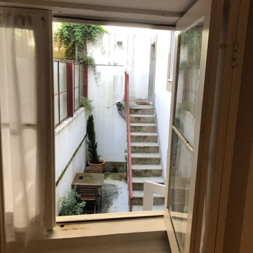 Vista do pátio PortoSense pela janela com escadas, corrimãos vermelhos e plantas em vasos no Porto