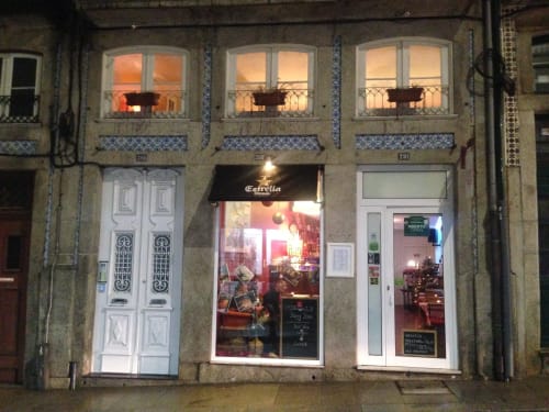Fachada da Estrella bar no Porto com vitrines iluminadas, detalhes em azulejo azul e iluminação quente ao anoitecer