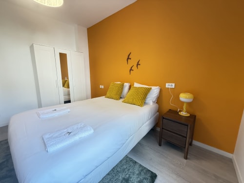 Chambre moderne avec mur d'accent doré-orange, lit blanc aux oreillers jaunes, table de nuit en bois et mobilier contemporain
