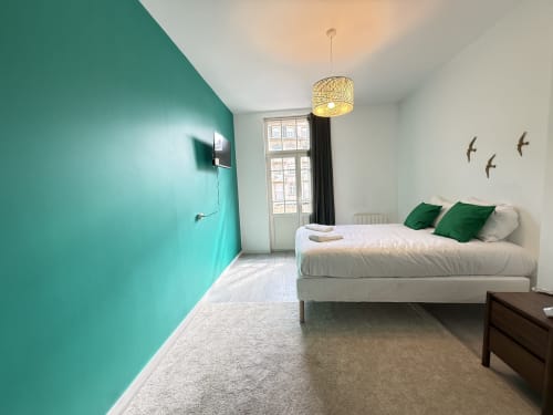 Chambre moderne de l'appartement Mattbnb Metz avec mur turquoise, balcon avec vue ville et coussins verts