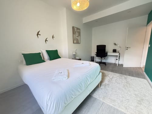 Chambre moderne dans un appartement de Metz avec lit queen-size, coussins verts, espace de travail et vue sur la ville