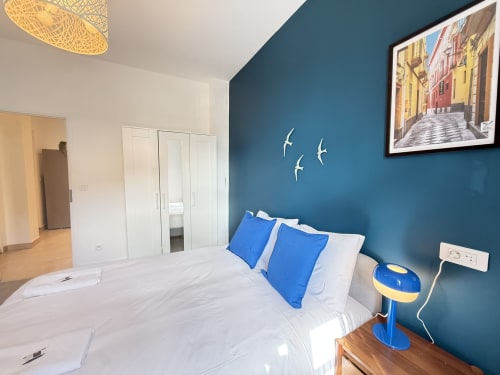 Chambre moderne à Metz avec mur accent bleu-vert, oreillers bleus, armoire blanche et vue urbaine