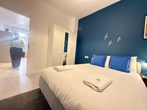 Chambre moderne avec lit blanc, mur d'accent bleu, décoration murale et accès ouvert à l'espace de vie de l'appartement Mattbnb Metz