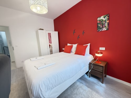 Chambre lumineuse avec mur d'accent rouge, lit blanc, oreillers rouges, table de nuit en bois avec lampe, armoire miroir et plafond tressé