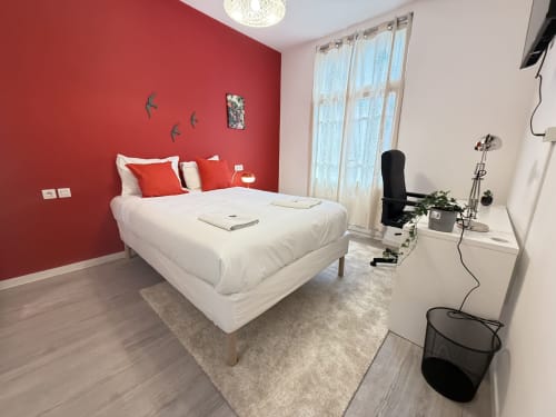 Chambre moderne dans un appartement messin avec mur d'accent rouge, lit blanc, coin bureau et vue sur la ville par grandes fenêtres
