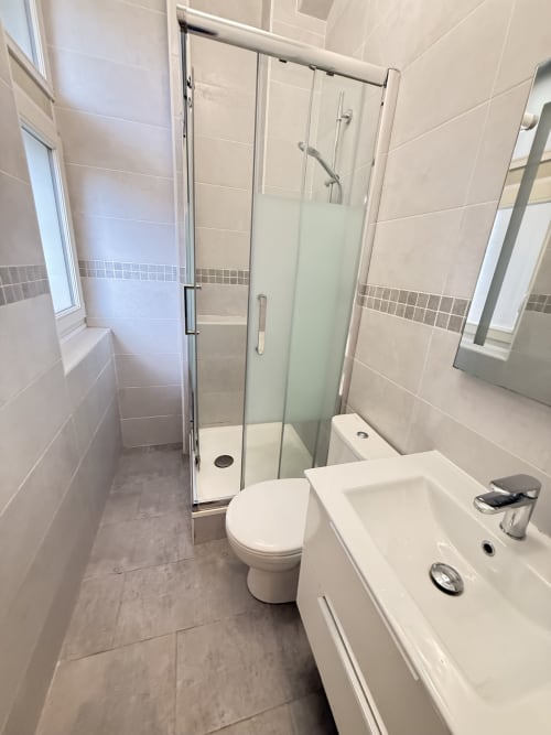 Salle de bain moderne avec douche à l'italienne, toilettes blanches, vasque et carrelage beige dans un appartement à Metz