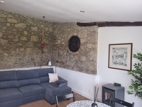 Sala de estar aconchegante em Casa Do Refúgio com paredes de pedra, sofá azul-marinho, lareira e vigas de madeira rústica