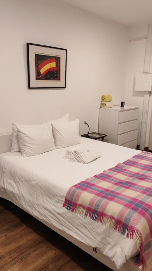 Quarto limpo na Casa Do Refúgio em Covilhã com roupa de cama branca, manta xadrez e obra de arte com bandeira espanhola