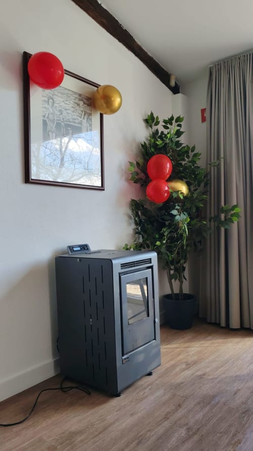Cantinho festivo no lobby da Casa Do Refúgio com balões vermelhos e dourados, planta em vaso e aquecedor de fogueira