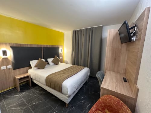 Chambre moderne du Norotel Brumath avec lit queen-size, mur accent jaune, TV écran plat et mobilier contemporain en bois