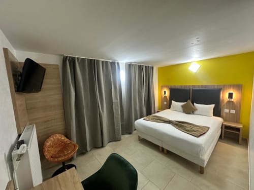 Modern double bedroom at Hôtel Norotel Brumath with bright yellow accent wall, white bed, and flat-screen TV in Brumath,