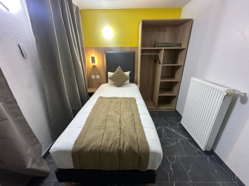 Chambre éco simple à l'Hôtel Norotel Brumath : lit étroit, tête de lit en bois, mur accent jaune, étagères et radiateur