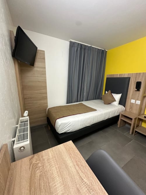 Modern hotel room at Norotel Brumath with single bed, yellow accent wall, and flat-screen TV in Brumath, France