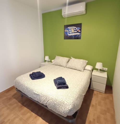 Modern bedroom in Mira Barna Barcelona apartment with green accent wall, cream bed, white nightstands, and air conditioning