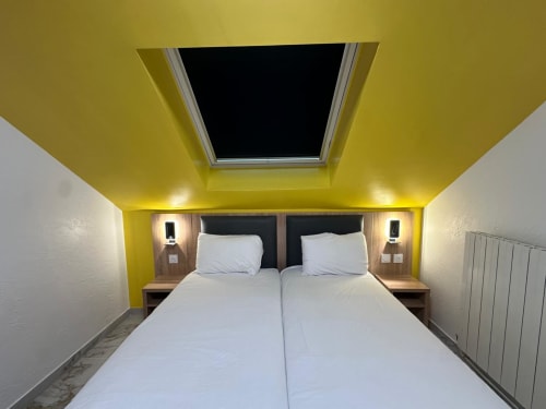 Chambre ensoleillée au plafond jaune vif de l'Hôtel Norotel Brumath avec lit double, puits de lumière et équipements modernes à Brumath, France
