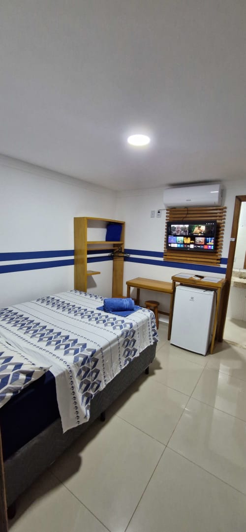 Compact private suite at Praieira Pousada&Hostel in Itacaré with blue and white decor, bed, TV, air conditioning, and mini