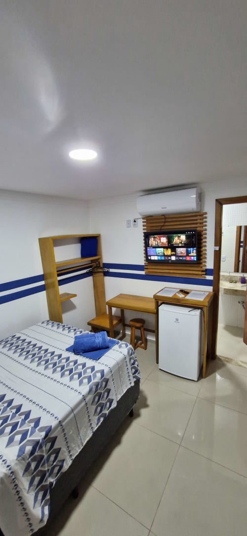 Compact private suite at Praieira Pousada in Itacaré with bed, TV, desk, and mini fridge