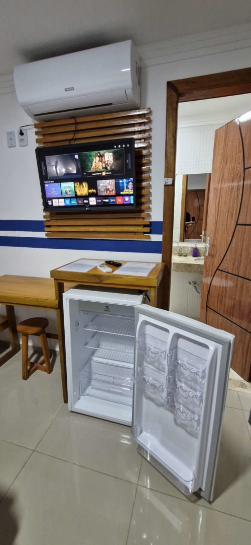 Open refrigerator in Suite Privativa Compacta at Praieira Pousada&Hostel, Itacaré, with TV and AC unit visible on wall behind