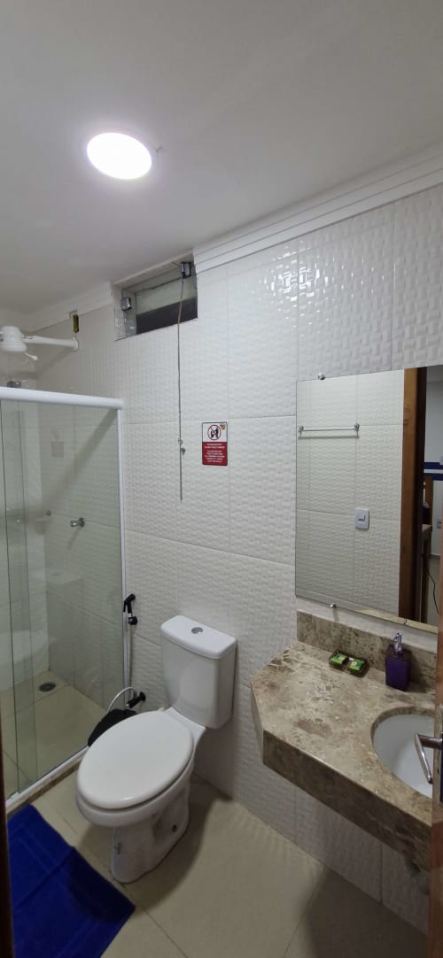 Modern bathroom in Praieira Pousada hostel, Itacaré with white tile walls, glass shower, toilet, sink and bright ceiling