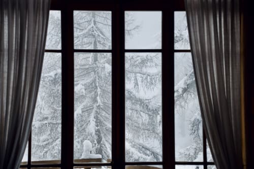Grande fenêtre aux rideaux gris encadrant des sapins enneigés à l'Hôtel De La Sage, La Sage