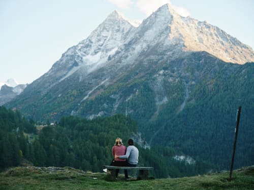 Deux clients admirent la vue sur les montagnes depuis un banc de l'Hôtel De La Sage à La Sage, Suisse