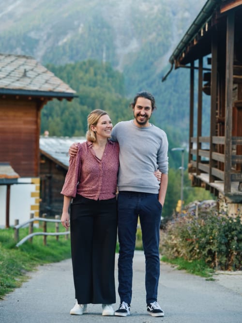 Couple souriant devant l'Hôtel De La Sage en montagne à La Sage, Suisse, entouré de paysages alpins