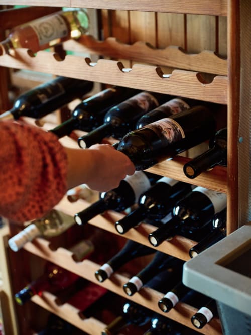 Main sélectionnant une bouteille de vin dans le casier en bois de l'Hôtel De La Sage, La Sage Suisse